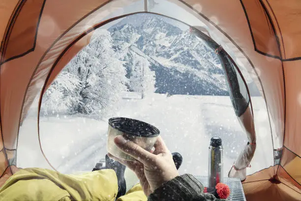 View from the tourist tent to the snow mountains. Guy in the boots lying at tent and drinking hot coffee. Collage. Travel concept