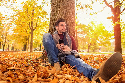 Handsome man taking a break at the park in autumn sitting on the ground