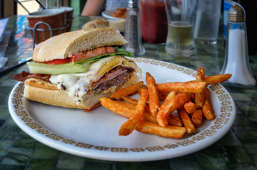 Half chivito sandwich, a popular dish in Uruguay, consisting in grilled beef, bacon, lettuce, tomato and egg; background of a  South American restaurant in California.