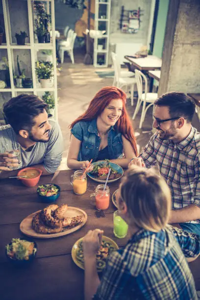 High angle view of small group of smiling people enjoying in conversation while having a healthy meal. Focus is on redhead woman.