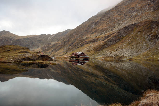 Nature landscape of amazing glacier lake Balea Nature landscape of amazing glacier lake Balea with house on shore and Fagaras mountains with white strips of snow reflected in the water at Carpathians, Romania balea lake romania stock pictures, royalty-free photos & images