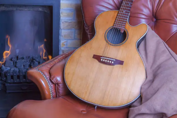 Relaxing winter hobbies. Acoustic guitar on armchair by the fire. Learning a musical instrument in the comfort of home.