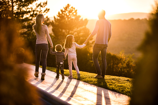 Rear view of a family holding hands and talking while taking a walk at sunset.