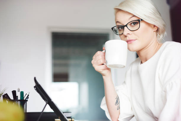 Close-up portrait of a smiling businesswoman sitting in front of computer and drinking a cup of tea.