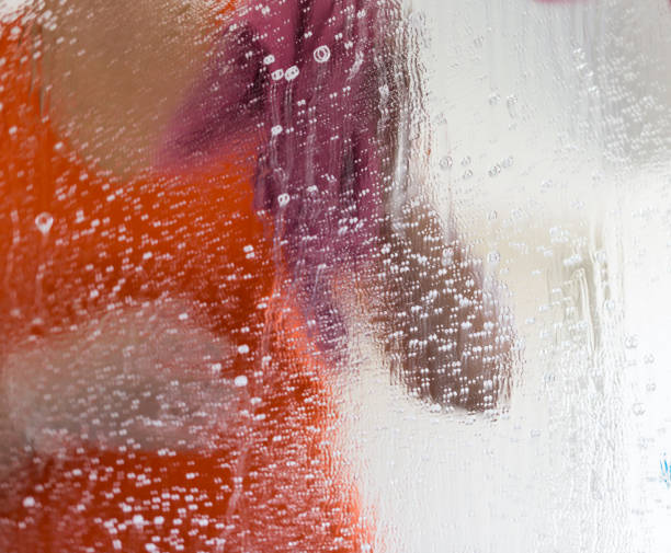 Woman in orange t-shirt cleaning a window stock photo