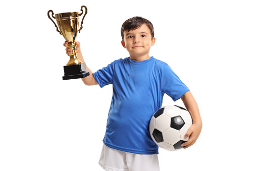 Little footballer holding a golden trophy isolated on white background