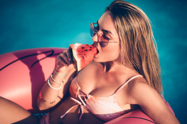 женщина в бассейне есть арбуз и плавающие на розовых надувных - sexy girl стоковые фото и изображения