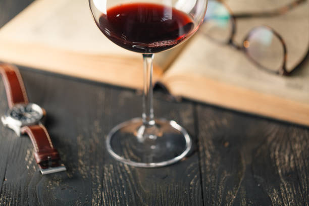 Red wine glass and old open book on wooden table