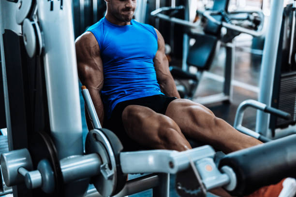 joven, ejercicio de piernas en el gimnasio local - máquinas de ejercicios fotografías e imágenes de stock