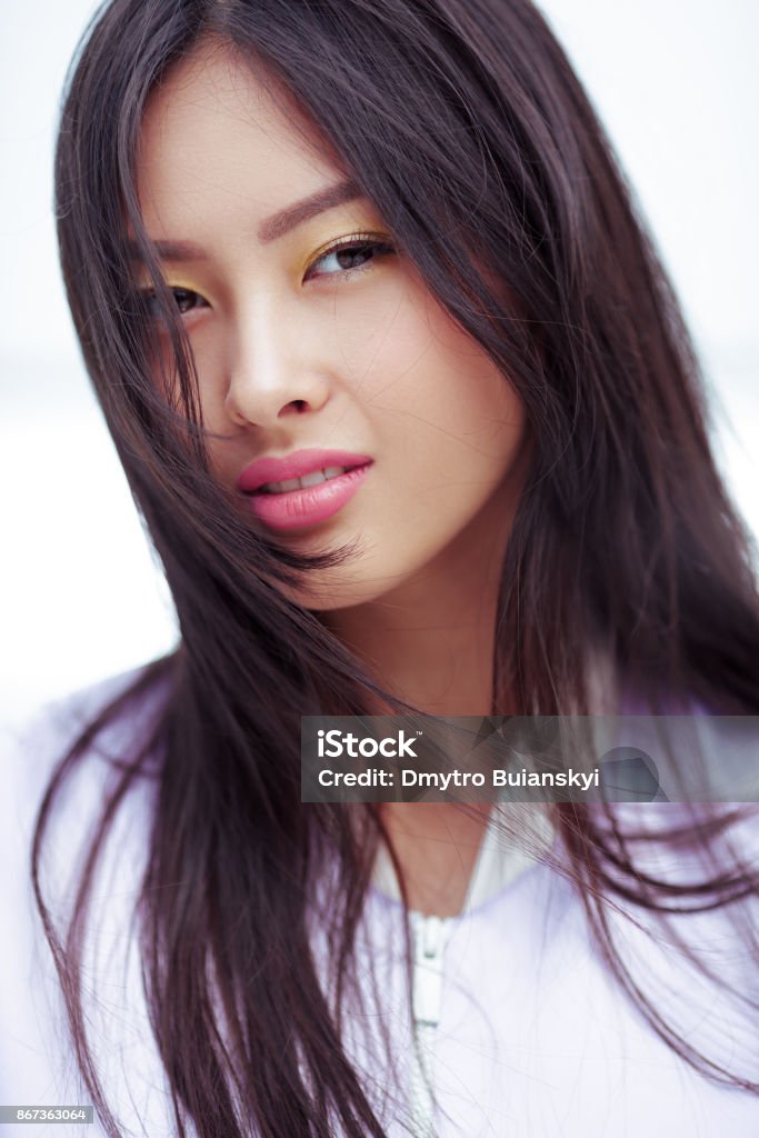 Asian fashion model outdoors Attractive asian woman smiling with elegant hairstyle and perfect soft colorful makeup. Skin care cosmetics concept portrait. Gorgeous models face with yellow pink make-up. Fashion shot outdoors against blue background Adult Stock Photo