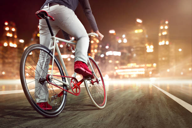 Person sitting on a modern single speed bicycle while resting one foot on the ground. In the background is a nightly skyline.