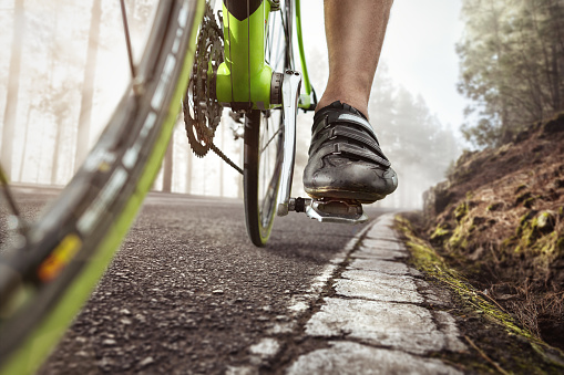 Pedal and shoe of a racing bicycle. Shot from a low angle with cracked road markings in the foreground.