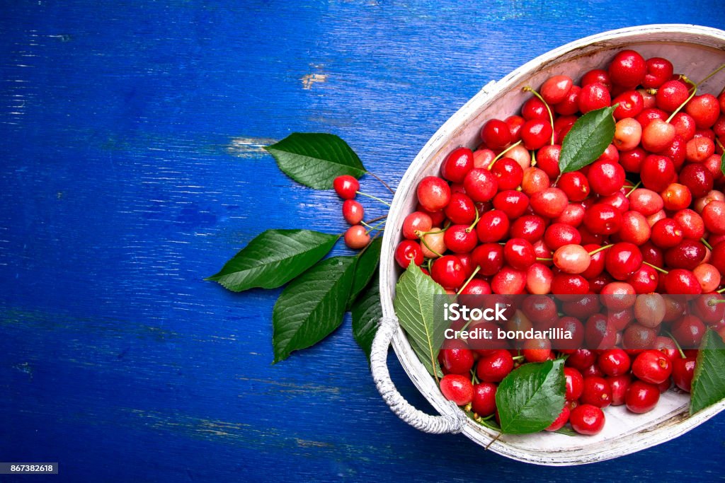 Cerezas rojas en canasta blanca sobre fondo azul madera. Cereza de cerca. Vista superior. Copia espacio. - Foto de stock de Agricultura libre de derechos