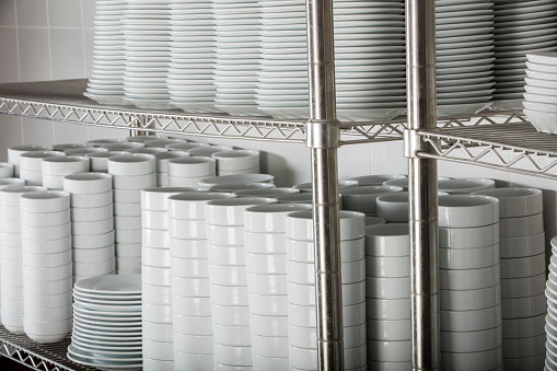 stacks of many white plates on a wire rack shelf in a commercial kitchen