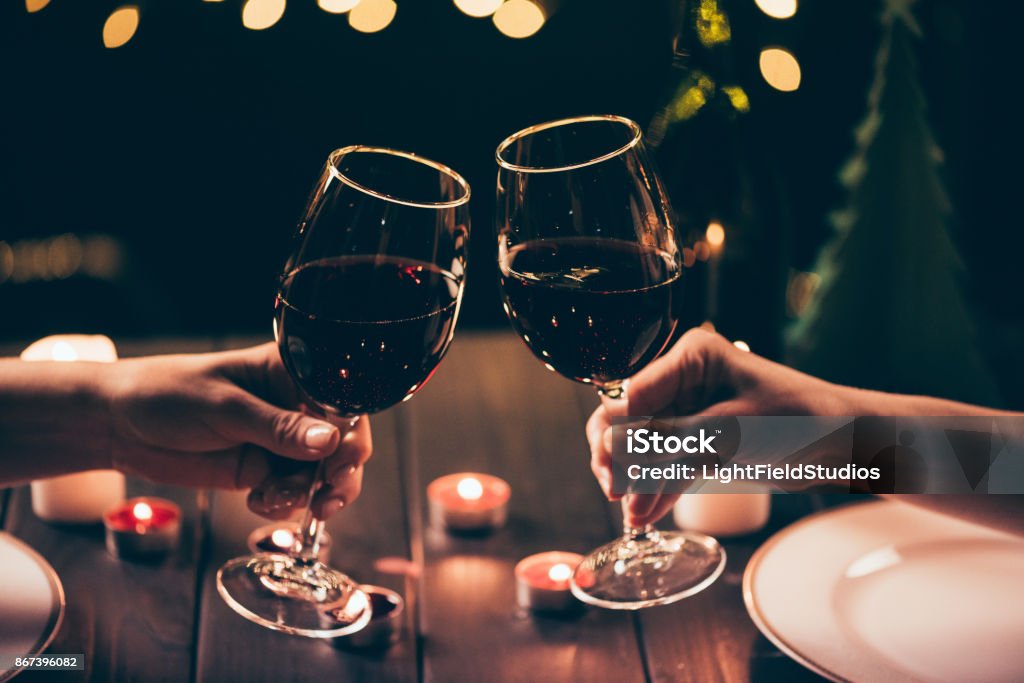 women clinking glasses over served table Cropped shot of two women clinking glasses with wine over served table with lit candles Wineglass Stock Photo