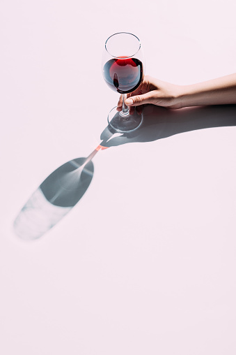 Cropped shot of woman holding glass of red wine over pink tabletop