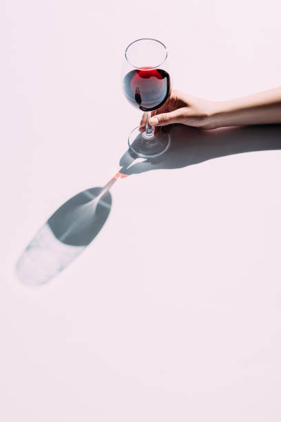 Female hand holding wineglass Cropped shot of woman holding glass of red wine over pink tabletop animal representation photos stock pictures, royalty-free photos & images