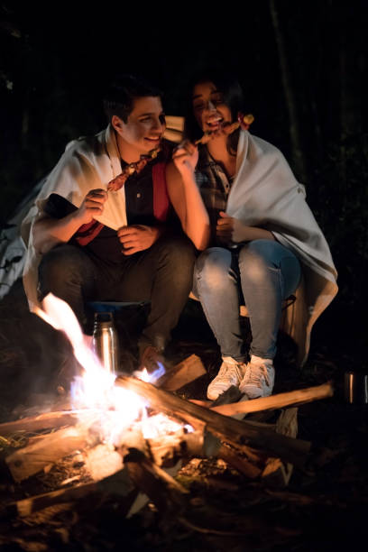 istock Couple outdoors sitting by a bonfire eating 867402082