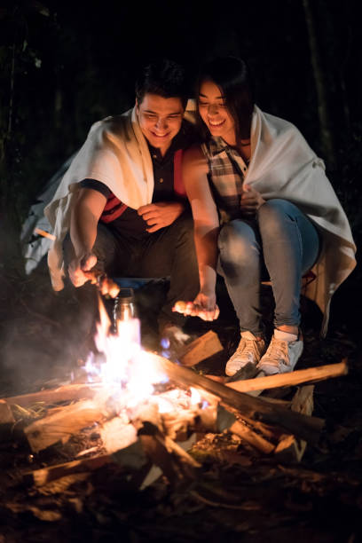 istock Happy couple outdoors sitting by a bonfire eating marshmallows 867402172