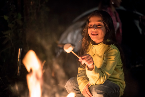 Portrait of a happy girl sitting outdoors by a bonfire eating marshmallows â outdoors lifestyle concepts