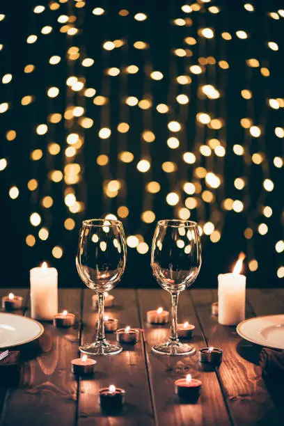 Two wineglasses on served wooden table surrounded by lit candles