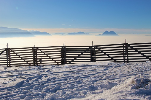 Fence in the snow and view of the alps, on the top of the mountain Gaisberg, height approx. 1300 m. A layer of high fog lies over the city of Salzburg. Austria, Europe.