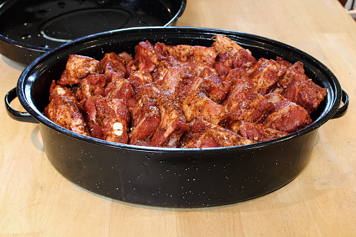 Ribs piled into a black roaster for slow cooking.