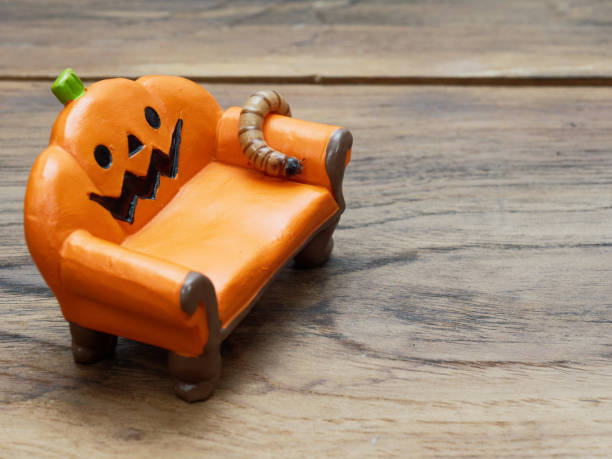 istock Super or giant worm crawling on orange miniature ceramic pumpkin couch or sofa over dark wooden surface 867454120