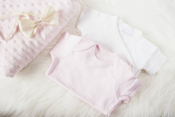 女の子のベビー服。ベビー ジャンプ スーツ、ロンパース、弓毛バンド、ピンクのおむつ。白い毛皮のカーペット。生まれたばかりの赤ちゃんのコンセプトです。赤ちゃんの女の子の服セッ� - onesie ストックフォトと画像