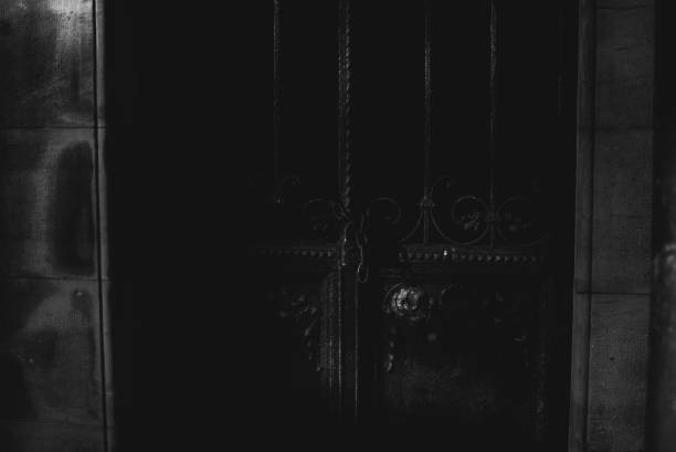 Black doors of the chapel with chains on the cemetery on sunny autumn aftetnoon.  Black and white