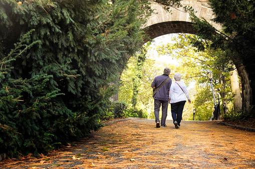 Senior couple discovering New-York City Fort Tryon park in Autumn. On this photograph, they walk under an arch hand in hand.