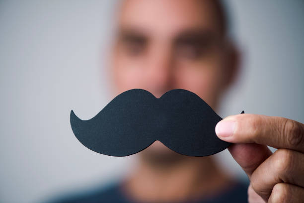closeup of a young caucasian man holding a fake moustache in front of his face