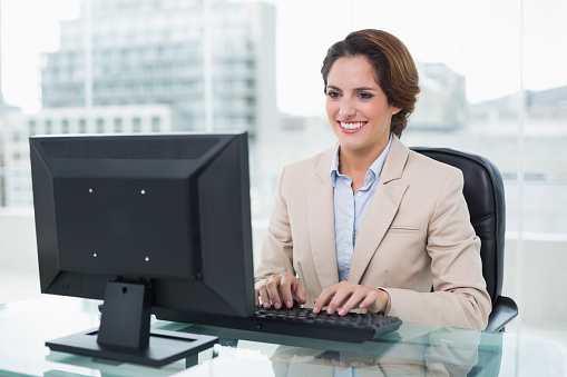 Cheerful businesswoman sitting in front of computer in bright office