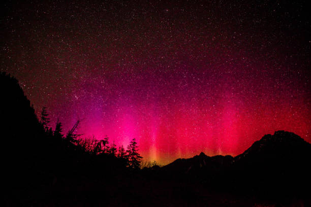 Radiant Night Sky Vivid magenta and red hue northern light sky with spectacular starry display over mountain and valley silhouette aurora polaris stock pictures, royalty-free photos & images