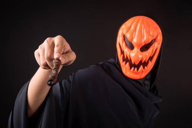 Mystery man with orange pumpkin evil mask holding magic wand on black background, Halloween night costume concept
