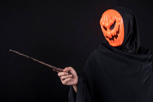 istock Mystery man with orange pumpkin evil mask holding magic wand on black background 867531192