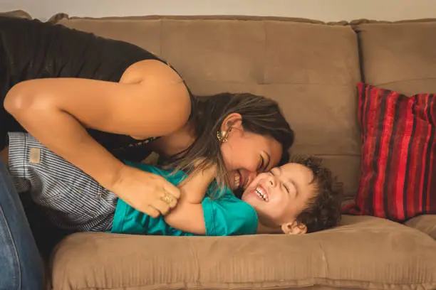 Mother and her child, tickling, kidding and having fun in the couch, with spontaneous smiles.