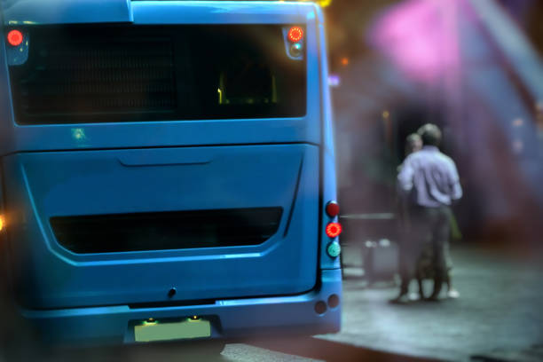 A bus on a bus stop is going to leave. Two men are waiting for the bus. Night in a city. Concept of transport in the night city, safety.