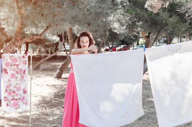 Housewife in the festive dress spreads the laundry and the linens on the wire to dry, looking at camera and smiling.