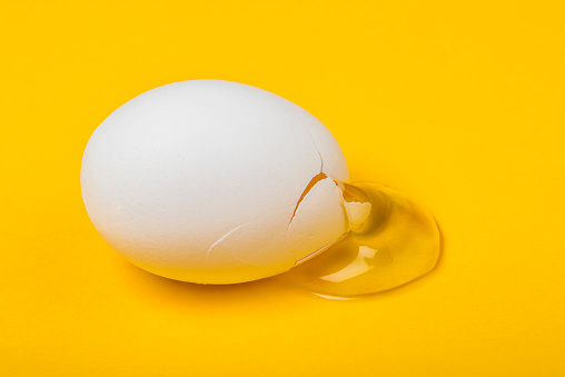 High angle view of cracked white egg with its yolk over yellow background. Horizontal composition. Image taken with Nikon D800 and developed from Raw format.