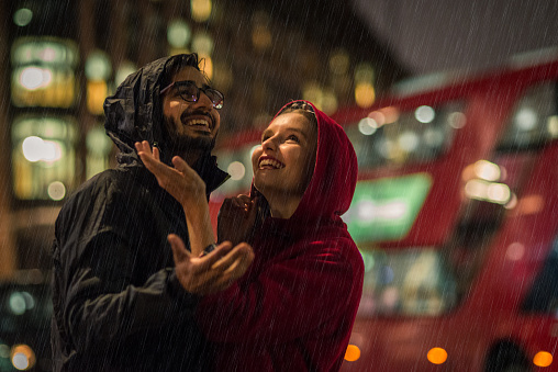 Young couple enjoying in the rain at night in London.