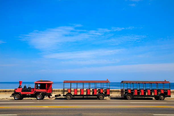 Red sightseeing roadtrain speeding along the Malecon in Havana, Cuba, motion blur, Caribbean Sea is visible in the background, 50 megapixel image.