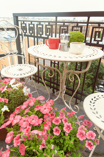 Coffee cups on table on small romantic balcony decorated with flowers outdoors