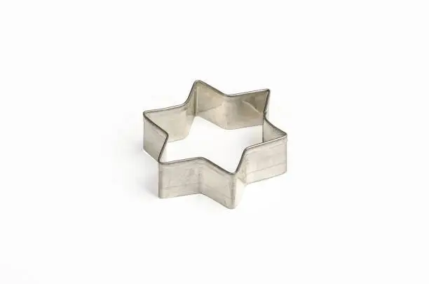 Star shaped Christmas cookie cutter over white. Tin biscuit cutter, a tool to cut cookie dough in particular shape and to make cutouts. Hexagram shaped and six pointed geometric star figure. Photo.