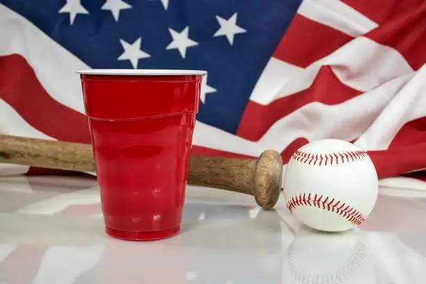 baseball and wooden bat with red party cup and American flag background