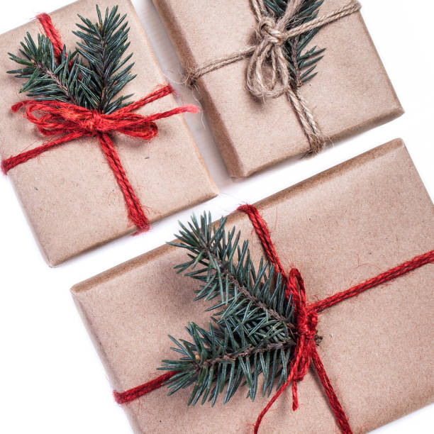 istock Festive boxes as Christmas present with ribbon bow and fir tree branch on white background wrapped in craft paper