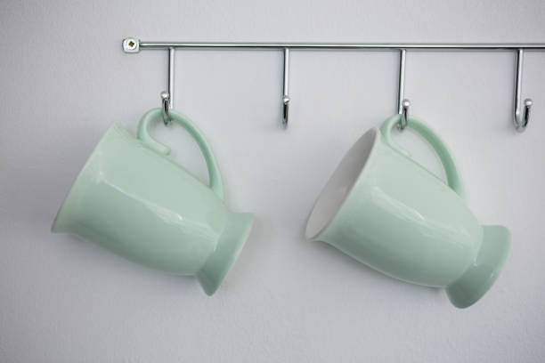 Close-up of mugs hanging on hook against white wall