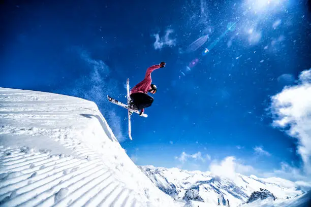 freestyle skier jumping of the kicker, blue background, against the sun