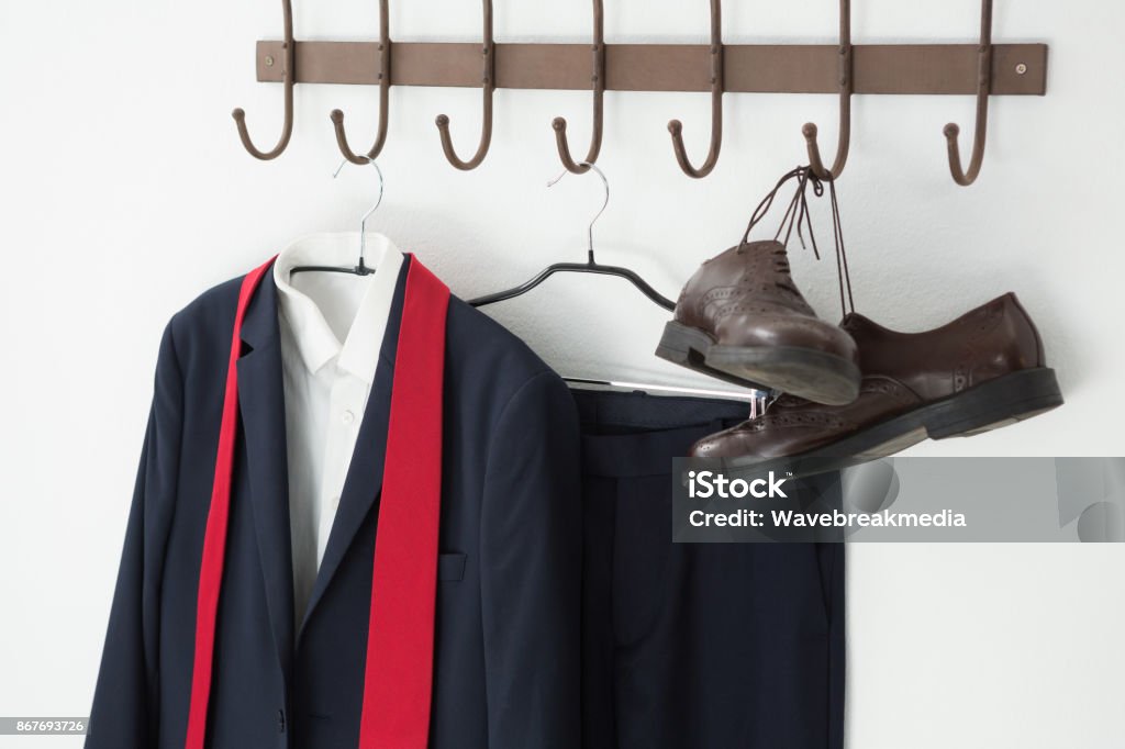 Close-up of full suit and shoes hanging on hook Close-up of full suit and shoes hanging on hook against white wall Absence Stock Photo