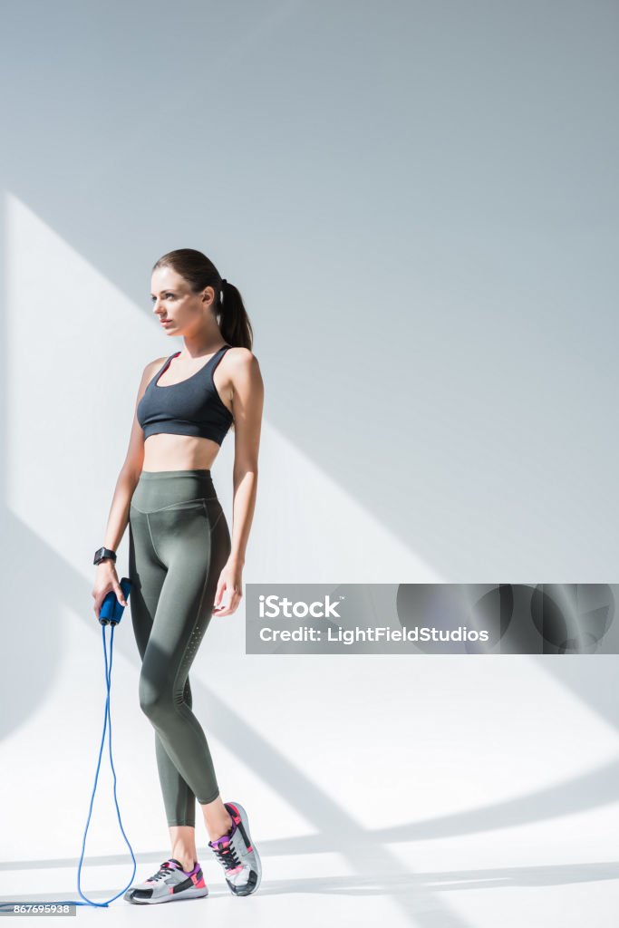 athletic girl with skipping rope athletic girl holding skipping rope and looking away on grey Jump Rope Stock Photo